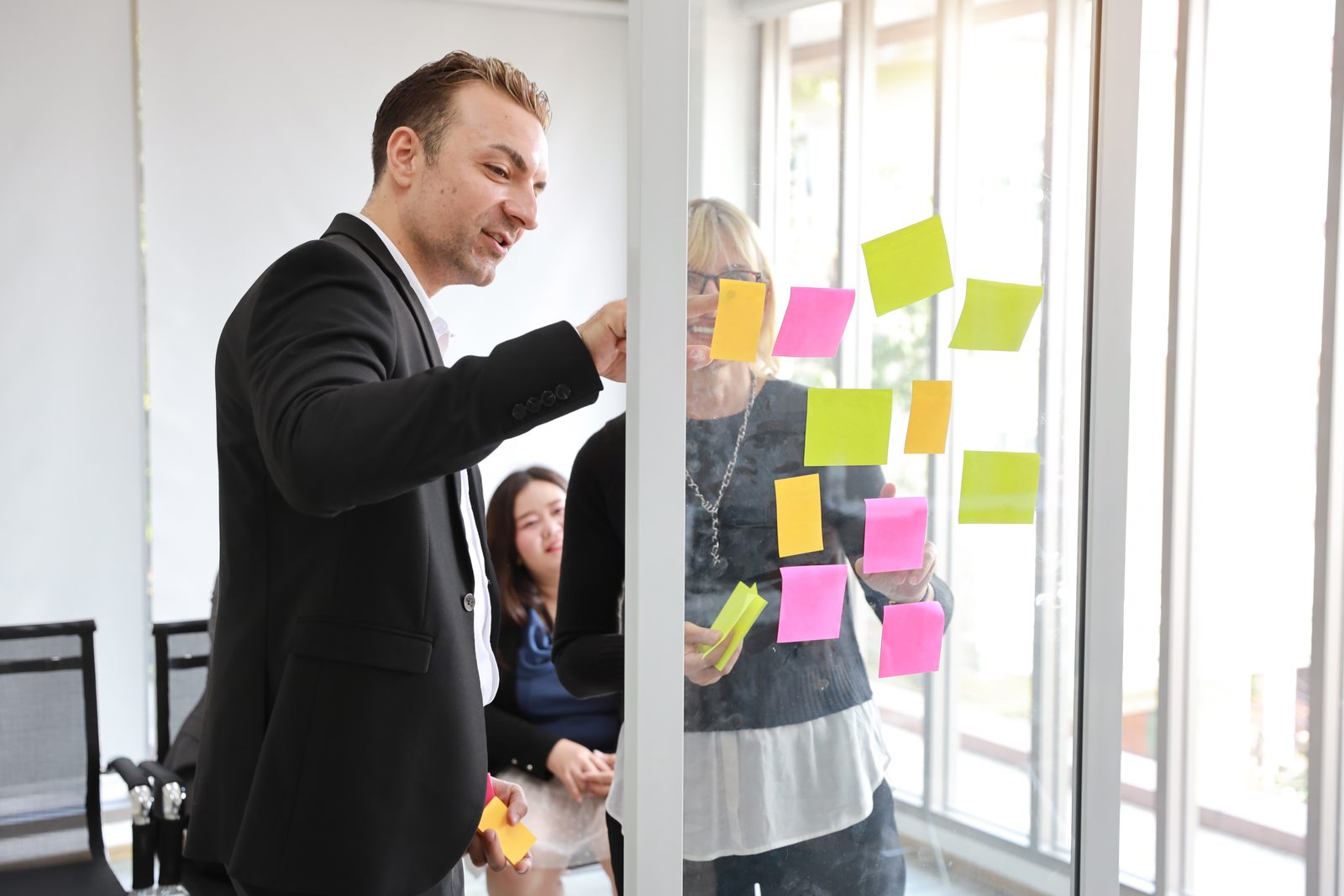 Executive leading a scenario planning workshop at a glass wall covered in sticky notes