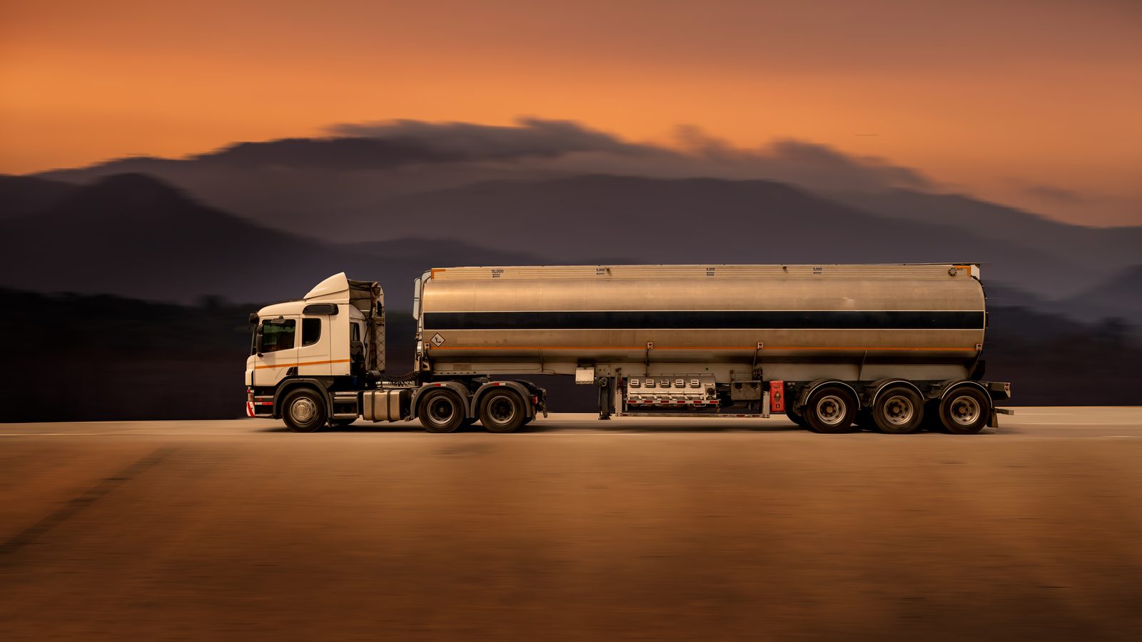 Fuel tanker truck on a road at dusk below mountains