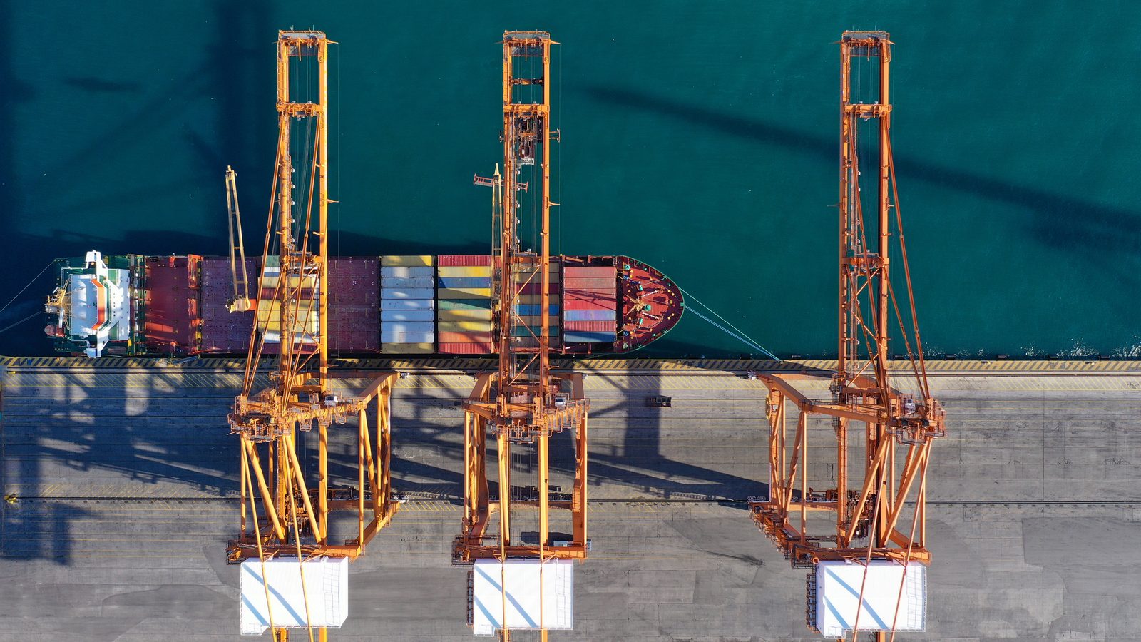 Aerial view of a cargo ship under container cranes at a port