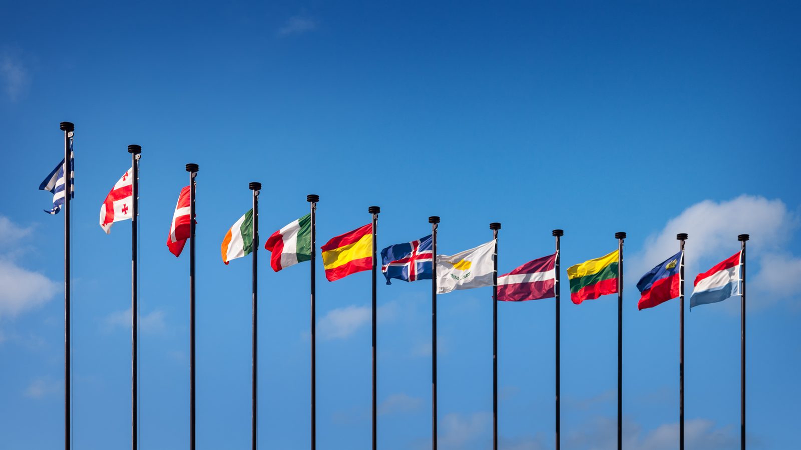 Row of national flags on flagpoles against a blue sky