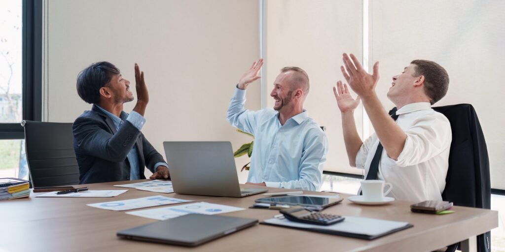 Executives high-fiving around a conference table, a picture of the easy agreement behind false consensus bias and groupthink