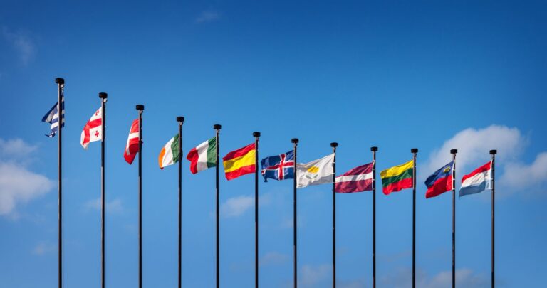 Row of national flags on flagpoles against a blue sky
