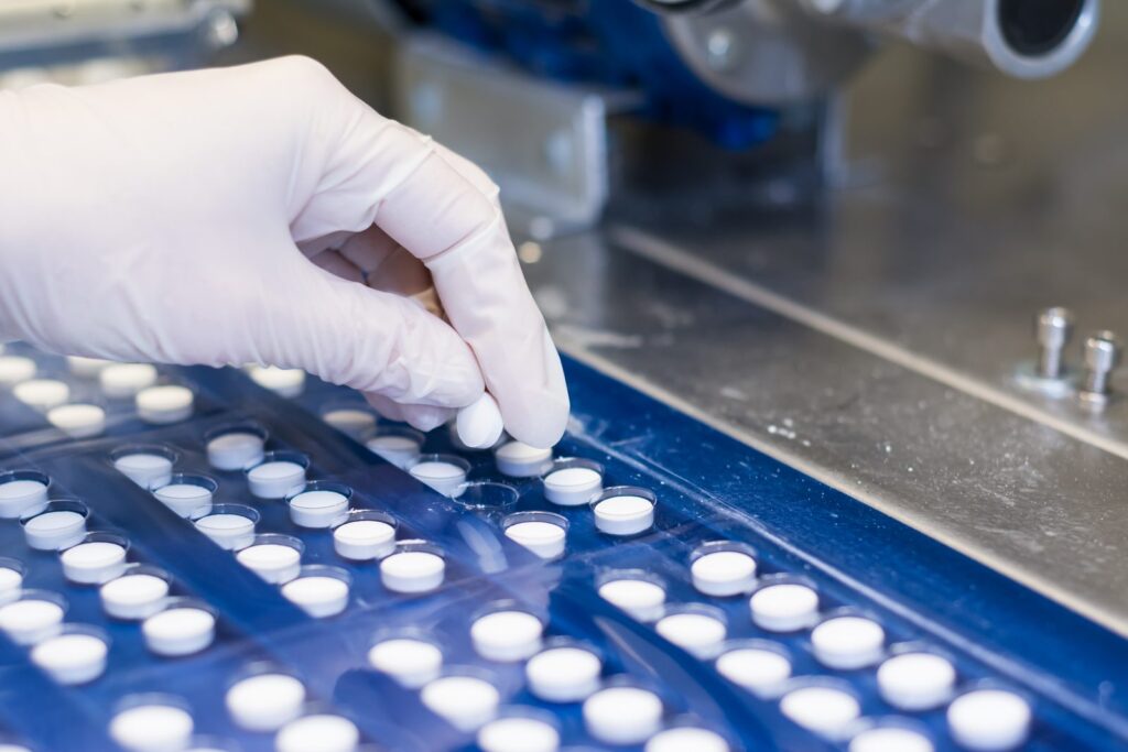 Gloved hand placing tablets into blister packaging on a production line, illustrating scenarios for the pharmaceutical industry