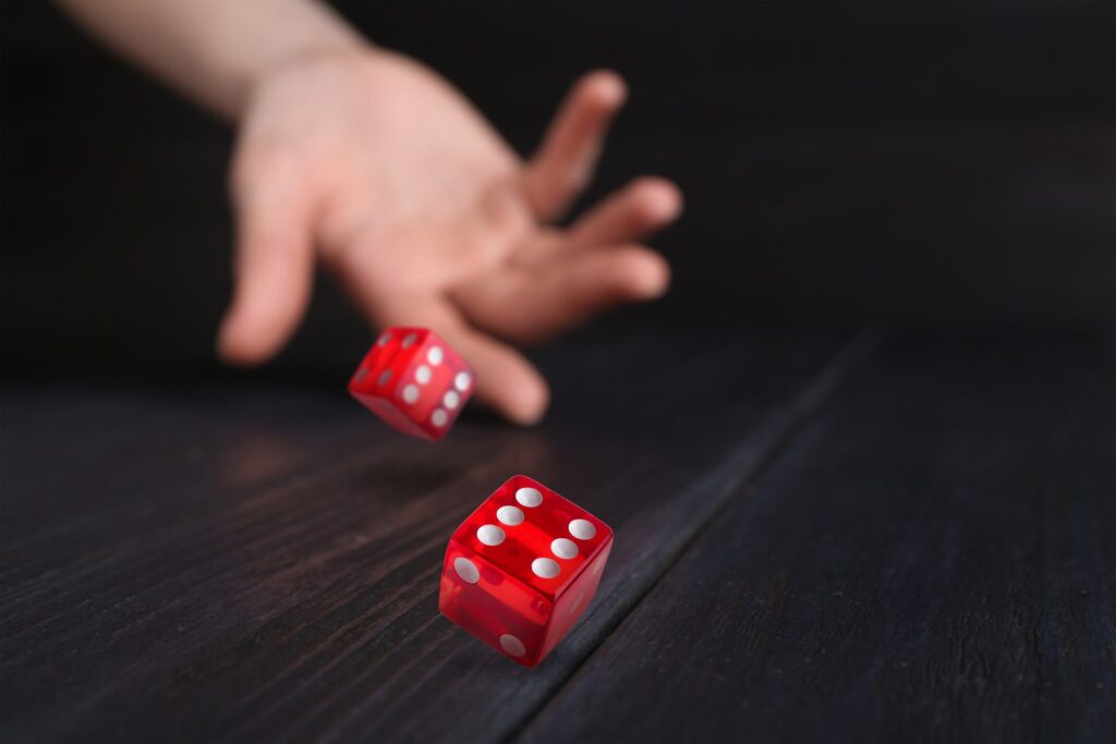 Hand rolling two red dice across a dark wooden table, a reminder that probability biases distort how we judge chance