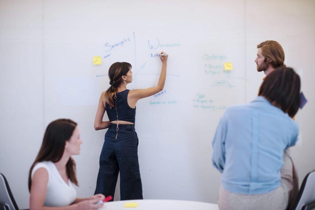 Analyst writing on a whiteboard as colleagues look on during a structured analysis session to reduce cognitive bias