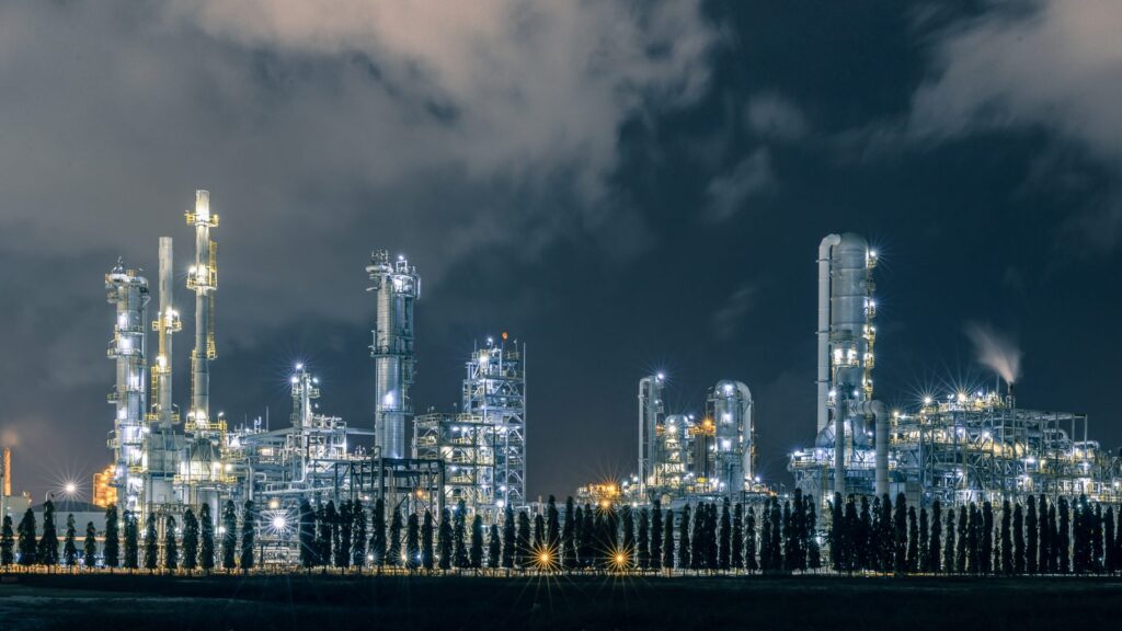 Oil refinery lit up at night under storm clouds, recalling Shell scenario planning before the 1973 oil crisis
