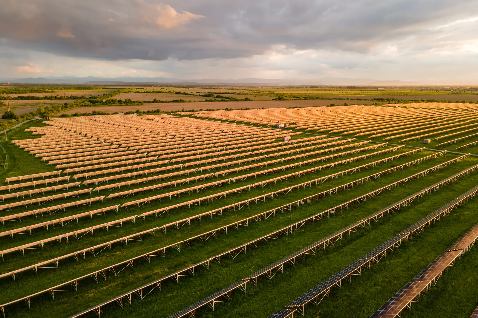 Aerial view of rows of solar panels stretching across a field at sunset
