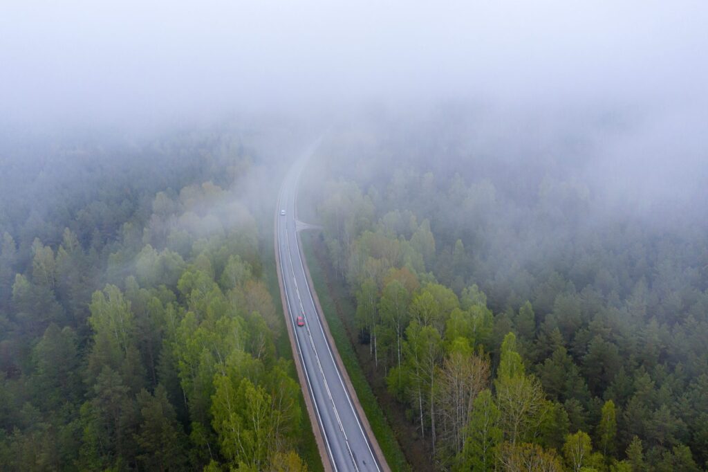 Aerial view of a road disappearing into fog through a green forest, symbolizing uncertainty in strategic foresight